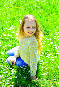 女孩坐在草地上的草地, 绿色的背景。鼎盛的概念。女孩在微笑的面孔花费休闲户外。儿童享受春天阳光明媚的天气, 而坐在草地上