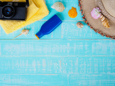 海滩配件，包括防晒帽，沙滩贝壳，黄色毛巾和复古相机，明亮的蓝色粉彩木背景，为暑假和假期的概念。