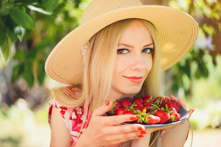 年轻的金发女人，在绿色花园的碗里放着草莓，一个夏天阳光明媚的日子，温暖的夏天，充满了形象自我关怀和健康的生活方式。