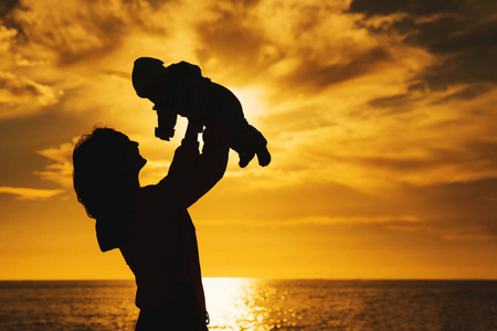 女人和她的孩子一起在海边户外玩耍. 年轻的母亲在天空中抛出婴儿.