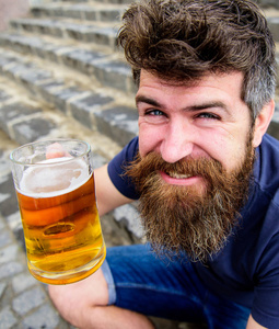 喝着啤酒休息的家伙。在欢快的笑脸上, 时髦的人喝着户外啤酒。庆祝概念。戴着胡子和胡子的男人坐在石梯上, 拿着啤酒喝着玻璃, 弥散