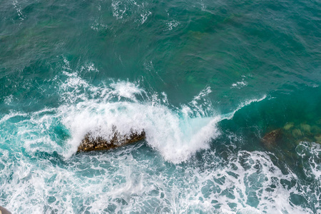 巨浪在岸上破浪前进。 波浪和白色泡沫。 沿海的石头。 从上面看。 海洋背景是绿色的