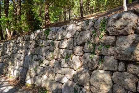 由粗糙的石头制成的旧石墙。 一种古老的坚固墙栅栏，有绿草和苔藓的图案。