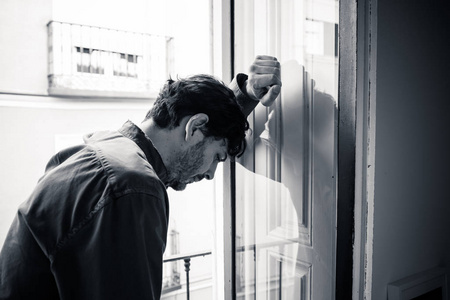 情感危机孤独的年轻人看着外面的房子,阳台上看着沮丧,摧毁了悲伤和