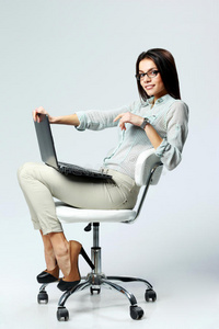 坐在办公椅上拿着笔记本电脑的年轻微笑的女商人