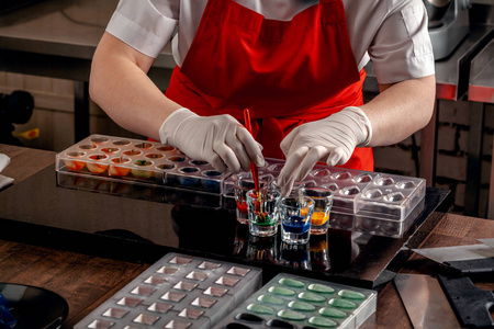 妇女糖果红色制服和白色手套做糖果在特殊形状从牛奶巧克力与可食用的油漆