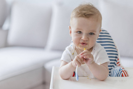 婴儿坐在高椅上，嘴里含着勺子吃着橙色的婴儿食品。小孩子坐在椅子上用勺子吃饭。家庭食物儿童饮食和父母观念