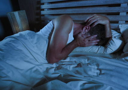 年轻的悲伤和绝望的男人躺在床上哭泣,沮丧地捂着脸,双手承受着抑郁和