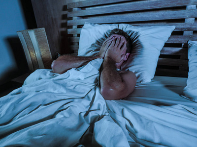 年轻的悲伤和绝望的男人躺在床上哭泣,沮丧地捂着脸,双手承受着抑郁和