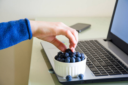 年轻的女人在家里用笔记本电脑吃蓝莓。