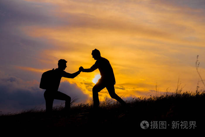 团队合作夫妇徒步旅行互相帮助信任协助剪影在山上日落团队合作的两个