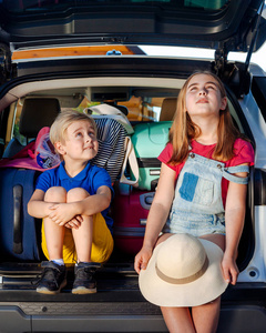 妹妹和哥哥坐在一辆车的后备箱里，提着手提箱。 乘车旅行家庭旅行一起度假。 笑的女孩和男孩准备和家人一起旅行。