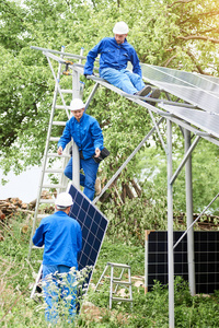 安装独立太阳能照片Voltaic面板系统。 戴安全帽和蓝色的工人在金属平台上整体提升太阳能组件。 替代能源和专业建设理念。