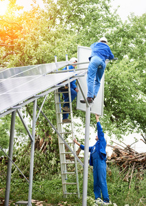 安装独立太阳能照片Voltaic面板系统。 戴安全帽和蓝色的工人在金属平台上整体提升太阳能组件。 替代能源和专业建设理念。