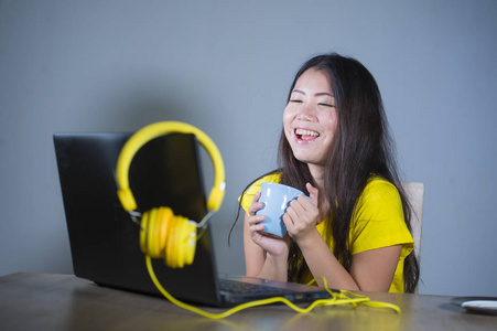 年轻漂亮快乐的亚裔韩国女性，在办公桌上享受互联网，在笔记本电脑上欢笑，快乐，在家喝茶，生活方式概念中的灰色背景