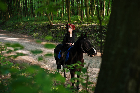 神秘的女孩在花环上穿黑色的马在木头上。