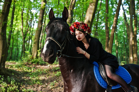 神秘的女孩在花环上穿黑色的马在木头上。
