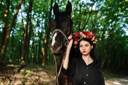 神秘的女孩戴着花环，穿着黑色的衣服，马穿着木头。