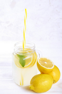 一个梅森罐杯自制的清爽柠檬水与有机成熟柠檬片，全和减半。无酒精饮料的乡村白色木制背景。特写，俯视图，复制空间..