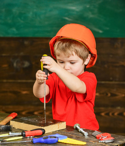 小男孩手持螺丝刀工具。幼儿在繁忙的脸上玩螺丝刀在车间。儿童在头盔可爱的发挥建设者或修理工, 或就要手工制作。就要手工制作和车间概