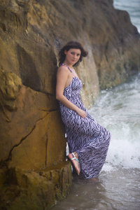 夏天，站在海洋背景的岩石附近的年轻女孩