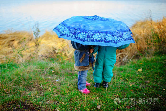 小女孩和男孩带着雨伞在雨中玩耍. 孩子们在秋天的雨天在户外玩耍.