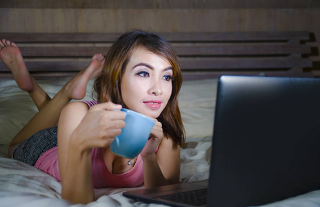 年轻美丽快乐的女学生，晚上在卧室里和朋友喝茶，用手提电脑看网络电影或视频聊天