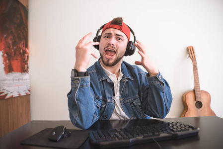 快乐的成年玩家留着胡子坐在舒适的房间里玩电脑游戏。耳机里的快乐男人在电子游戏中为胜利而高兴。玩家概念
