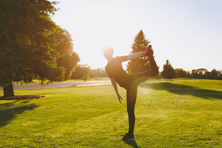 年轻的运动女孩穿着黑色制服帽,做运动锻炼,热身伸展,然后在阳光明媚