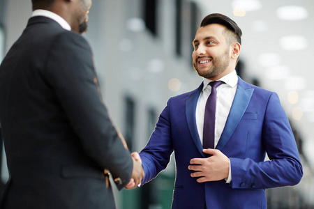 穿西装的年轻雇员在机场开会时与外国同事握手照片