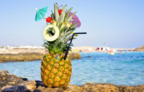 菠萝装饰在一个伟大的异国风格与水果和迷你伞。 背景上的石头和海水。 文本的负拷贝空间位置。 尼西海滩阿伊亚纳帕塞浦路斯。