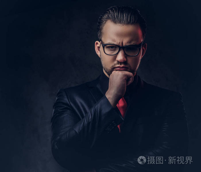 穿着黑色西装和红色领带的沉思时尚男性的肖像孤立在黑暗的背景上