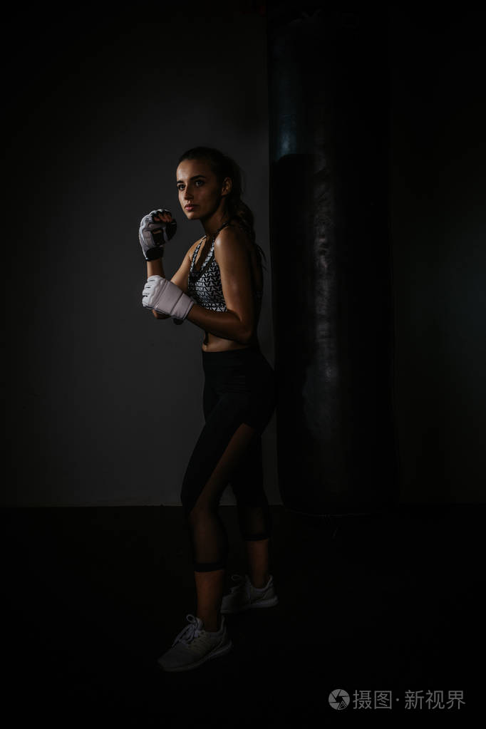 年轻漂亮的拳击手在黑暗的健身房里