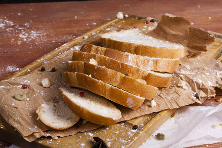新鲜而芬芳的白色面包被切成薄片，躺在木制的背景上。 一点香料已经添加到它，它也在牛皮纸上。 无麸质。 概念食品照片。