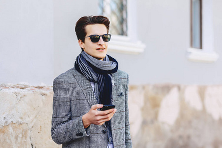 时尚的年轻人戴着太阳镜，带着电话走在街上