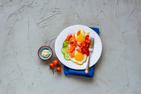 健康的早餐在平铺的盘子里。烟熏三文鱼，煎蛋，西红柿和黄瓜在浅混凝土背景俯视图。好脂肪健康饮食理念。