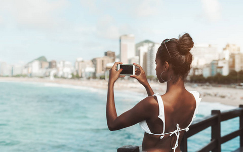  rear view of a young svelte black female with a smartphone phot