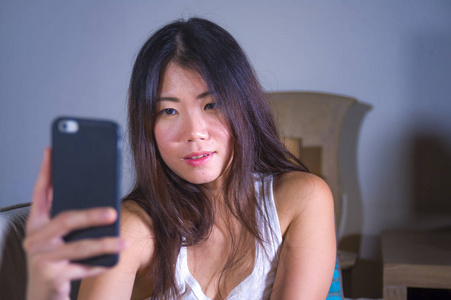 年轻甜美快乐美丽的亚洲女性，用手机为网络社交媒体自拍，在手机上笑，在家在线交流生活方式概念