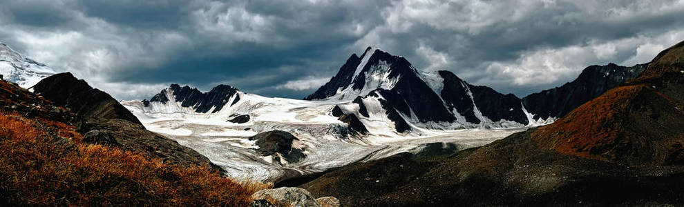 美丽的戏剧性的山风景。黑暗的山脉和冰川在乌云密布的背景下。全景背景