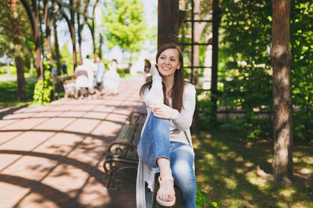 美丽的白种人年轻女子的肖像，带着迷人的微笑，穿着轻盈的便服。 微笑的女性坐在拱门下，在城市公园的街道户外春天的自然。 生活方式概
