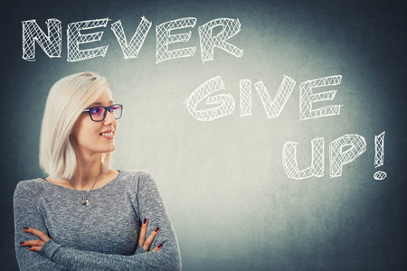 自信的年轻女子的肖像,交叉双臂,戴着灰色墙壁背景的眼镜,文字永不