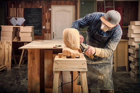 有经验的木匠穿着工作服，小木匠老板在木工车间工作，用角磨机在桌子上加工板是锤子和许多工具