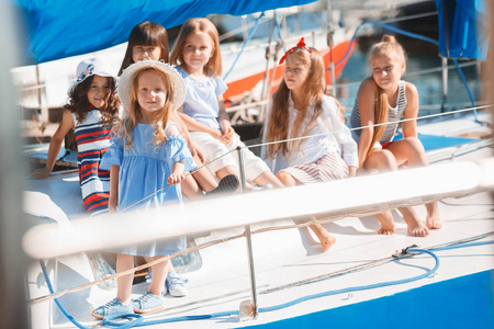 海上游艇上的孩子们喝橙汁。 青少年或儿童女孩对抗蓝天户外。 五颜六色的衣服。 孩子们时尚阳光的夏季河流和假日概念。