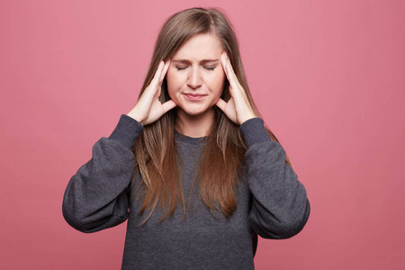 人烦恼欧洲女人的肖像头痛,双手放在太阳穴上,闭上眼睛,穿着随意,孤立
