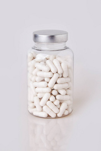 维生素抗生素白色软明胶胶囊在透明玻璃瓶中分离在白色背景上.