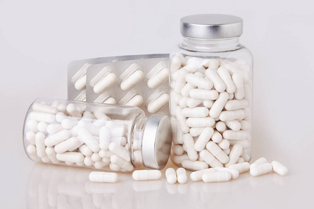 白色软明胶胶囊在透明玻璃瓶与一些分散的桩分离在白色背景.