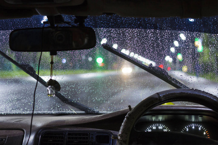 在夜间城市的雷雨和雨中，玻璃清洁剂打开了汽车挡风玻璃上美丽的水滴。 前后背景模糊