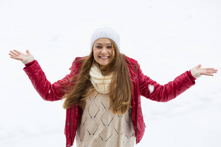 一个金发的年轻漂亮女孩喜欢第一场雪。 红色夹克，白色帽子和手套。 冬天的时候。