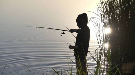 湖岸上有一个拿着鱼竿的人在钓鱼。 太阳下湖岸的渔民。