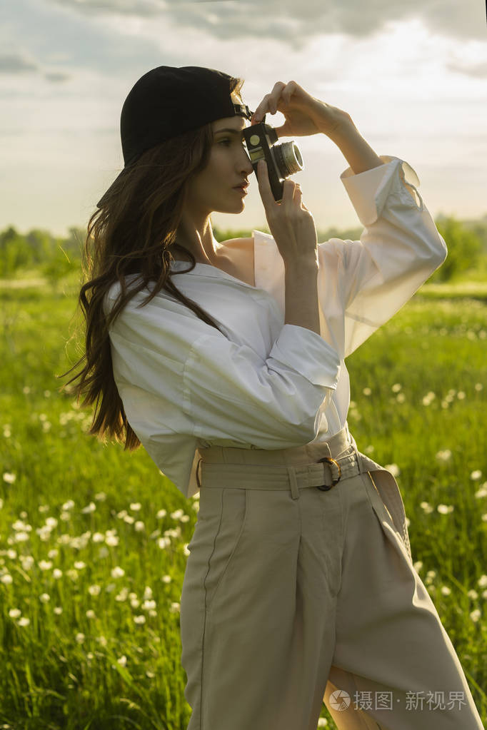 米色裤子,在户外摆姿势,在日落光线下,一个充满鲜花的草地背景下,用
